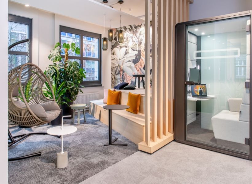 Modern gestaltete Bürofläche mit Lounge-Bereich, bepflanzten Zonen und integrierter Telefonbox für ruhige Zusammenarbeit und Rückzug im Arbeitsalltag.