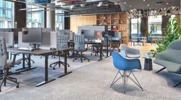 Open-Space-Büro mit höhenverstellbaren Arbeitsplätzen, zonierten Arbeits- und Loungebereichen sowie flexiblen Zonen für Austausch und Rückzug.