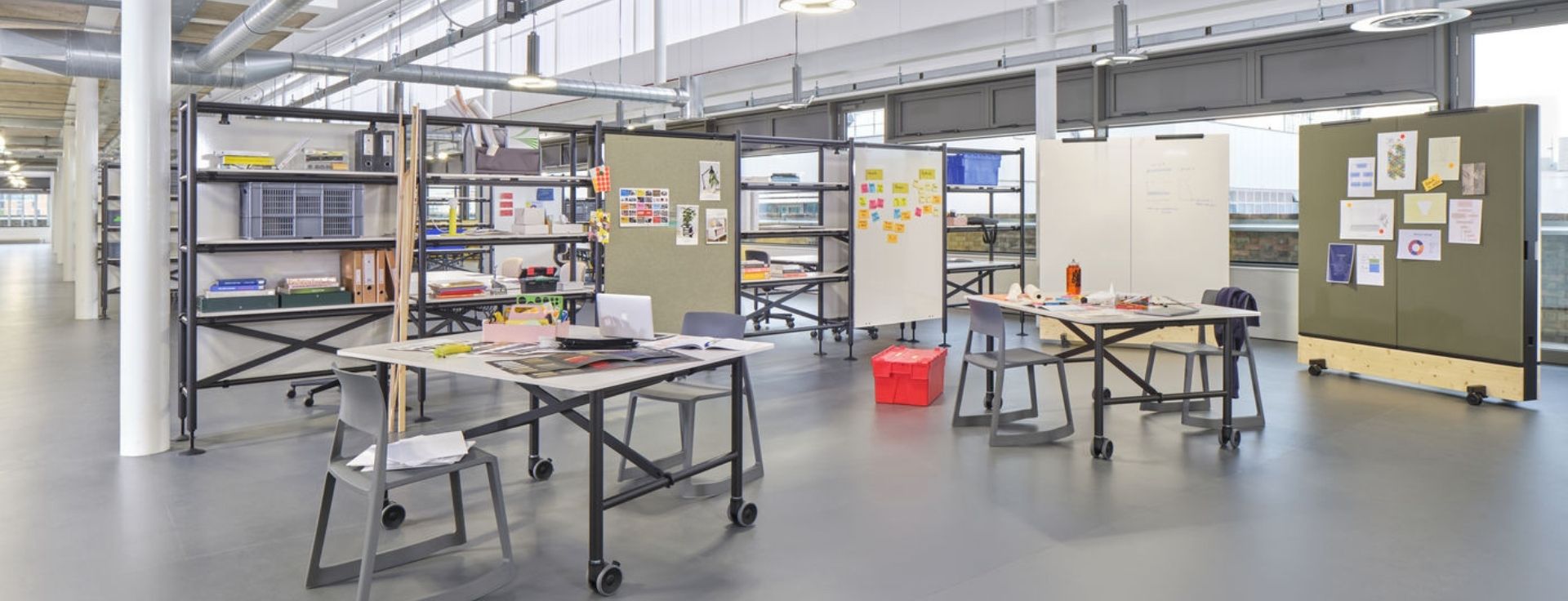 Flexible Arbeitszone mit mobilen Tischen, freistehenden Stellwänden und Whiteboard‑Elementen in einem offenen Büro.