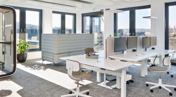 Moderne Bürofläche mit höhenverstellbaren Schreibtischen, Monitorarbeitsplätzen, einer schallgedämmten Telefonkabine und abgeschirmten Sitzbereichen vor großen Fensterfronten.