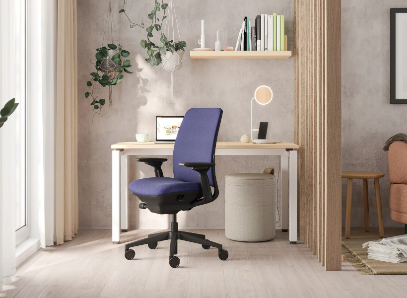 Modernes Homeoffice mit ergonomischem Drehstuhl, hellem Schreibtisch, minimalistischer Tischleuchte, Wandregal und Pflanzen vor einer strukturierten Betonwand.