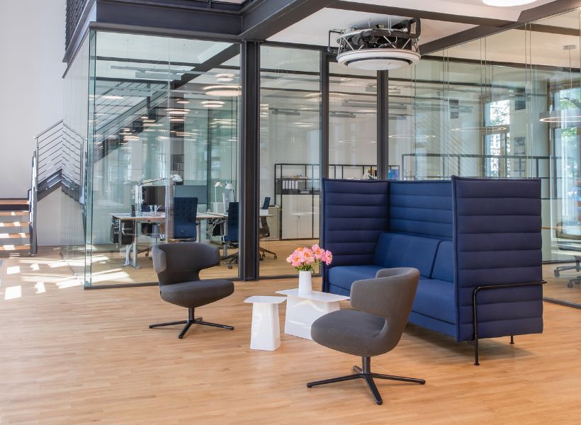 Offene Wartezone mit zwei Sesseln, abgeschirmter Sitznische und Beistelltisch vor verglasten Büro- und Besprechungsräumen.