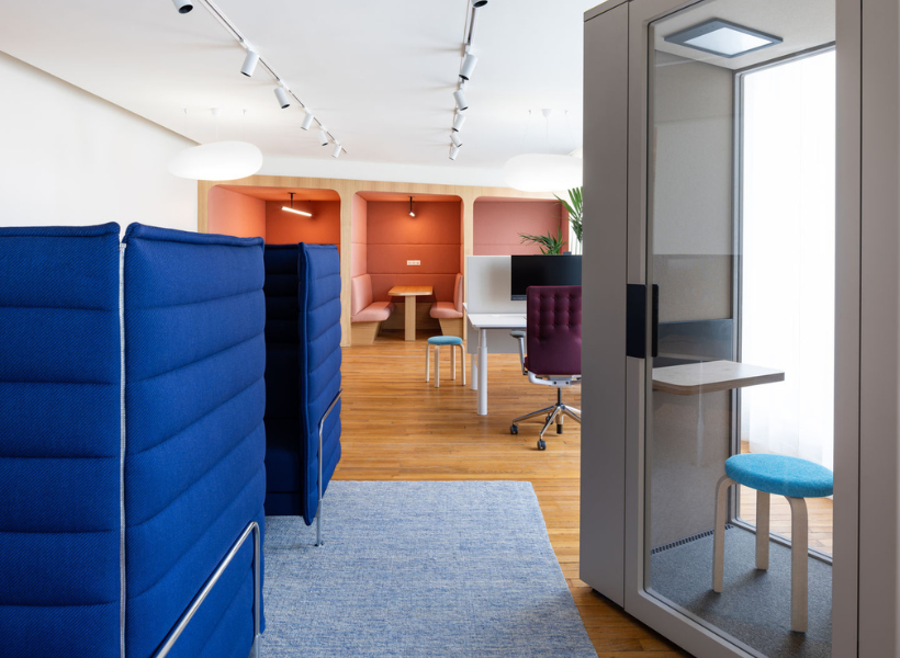 Modernes Büro mit akustisch gepolsterten Fokusbereichen in kräftigen Farbtönen, einer kleinen Telefonbox und einem zentralen Arbeitsbereich.