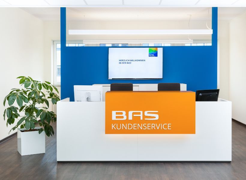 Empfangsbereich mit zentraler Empfangstheke, Bildschirmarbeitsplätzen und digitaler Begrüßungsanzeige hinter dem Tresen.