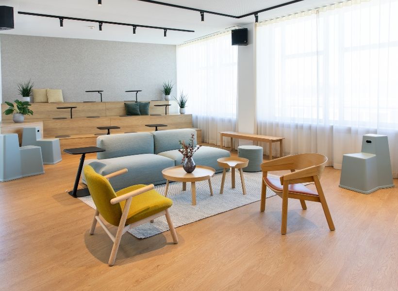 Multifunktionaler Besprechungs- und Lounge-Raum mit Podest, hellen Holzelementen und weich gepolsterten Sitzmöbeln für flexible Nutzung.