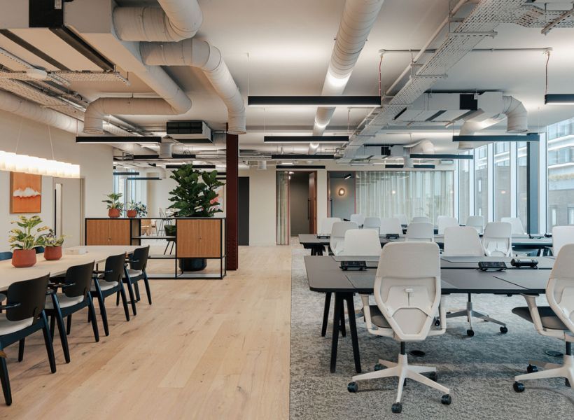 Modernes, offenes Büro mit Schreibtischen, weißen Drehstühlen, Lounge‑Bereich und Pflanzen.