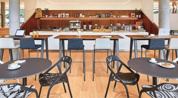Großzügiges Workcafé mit Kaffeebar, Stehtischen, Sitzgruppen und Arbeitsplätzen mit Laptops als Kombination aus Begegnungs- und Arbeitsbereich im Büro.