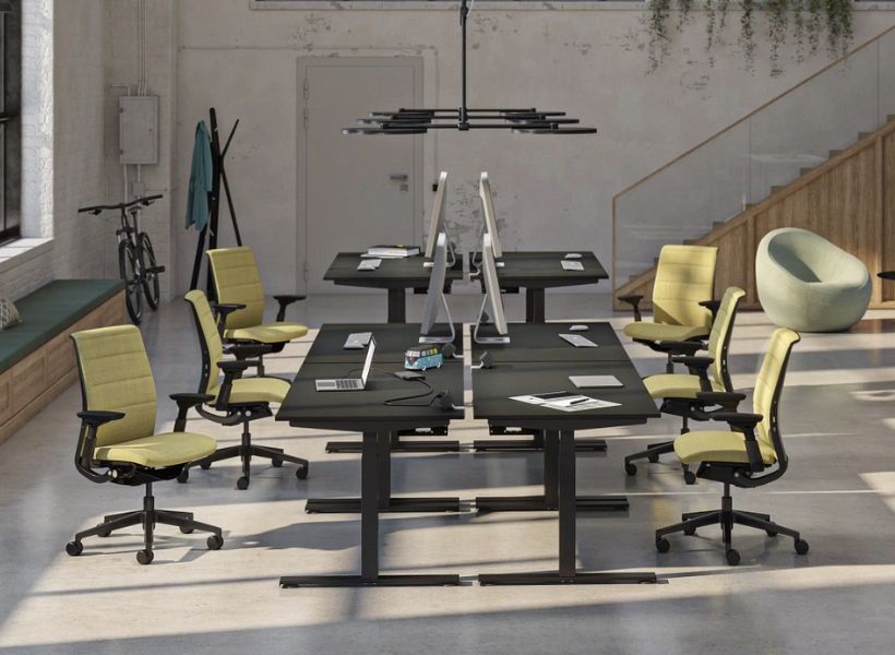 Offener Bürobereich mit großen Schreibtischen, ergonomischen Drehstühlen und heller Industriearchitektur.