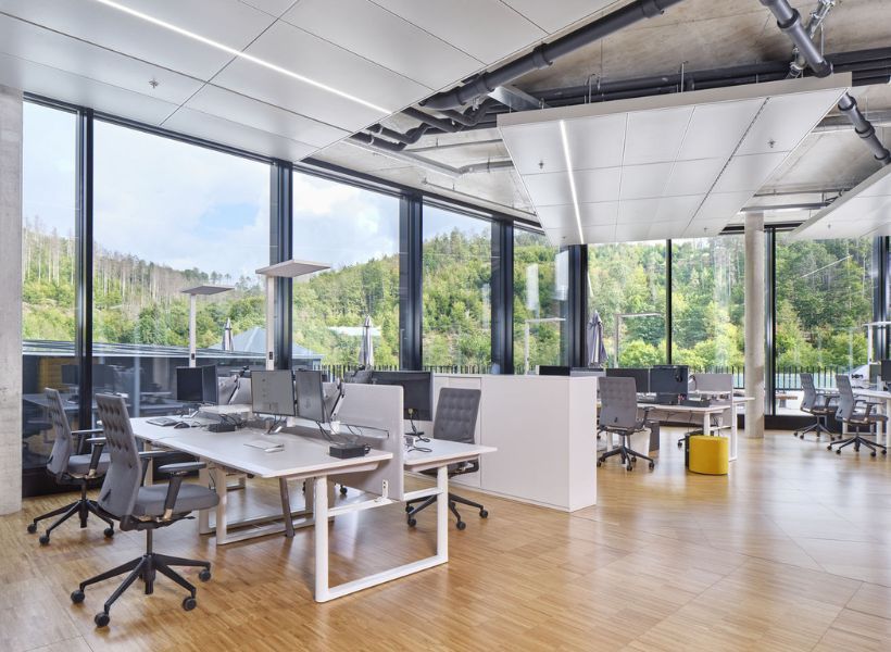 Arbeitsbereich mit mehreren Schreibtischen, Bürostühlen, Monitoren und gepolstertem Raumteiler in offener Bürogestaltung.