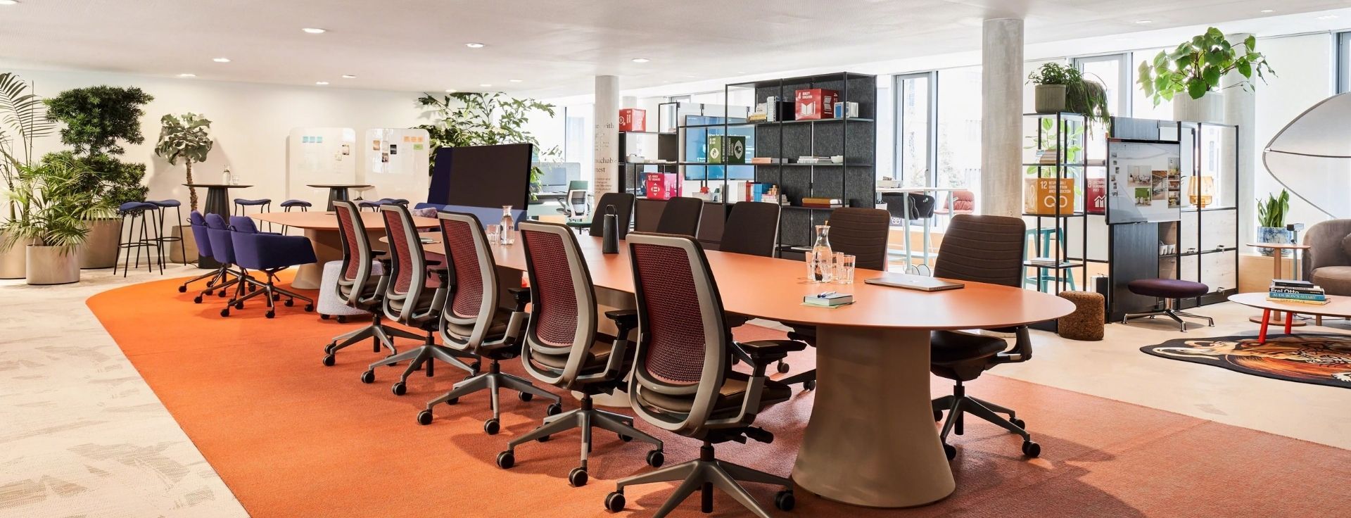 Großer Besprechungsraum mit langem Tisch, ergonomischen Drehstühlen und offenem, modern eingerichteten Office‑Bereich.