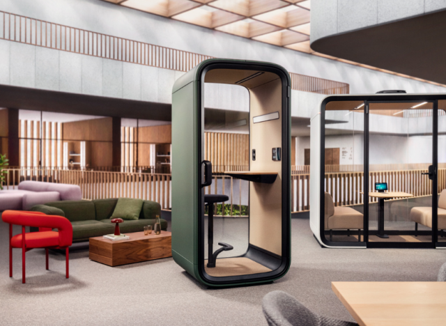 Gemütliche Büro-Loungezone mit gepolsterten Sesseln, Pflanzen, offenem Regalsystem und angrenzendem Konferenzraum.