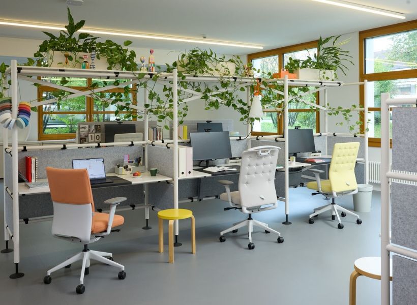 Moderne Büroarbeitsplätze mit Tischtrennwänden, ergonomischen Stühlen und Pflanzenelementen zur Strukturierung des Open Space.