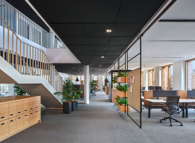 Offener Bürobereich mit großen Schreibtischen, ergonomischen Drehstühlen und heller Industriearchitektur.