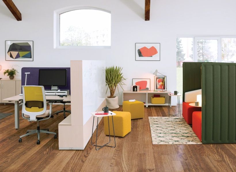 Heller Bürobereich mit Arbeitsplatz, Loungemodulen, farbigen Sitznischen und dekorativen Elementen.