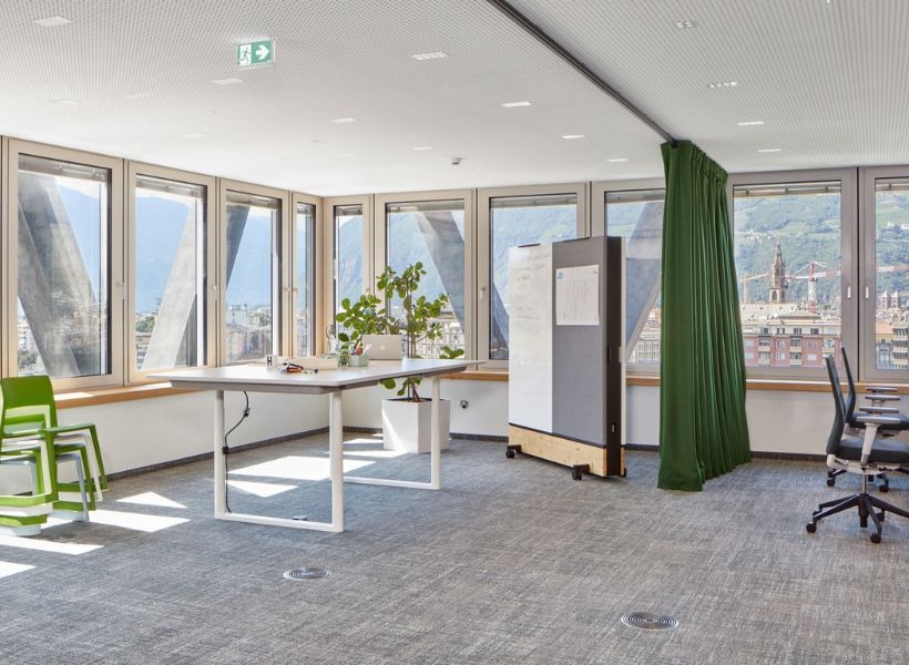 Heller Büroraum mit mobiler Stellwand auf Rollen und Vorhang zur flexiblen Abtrennung von Arbeitsbereichen.