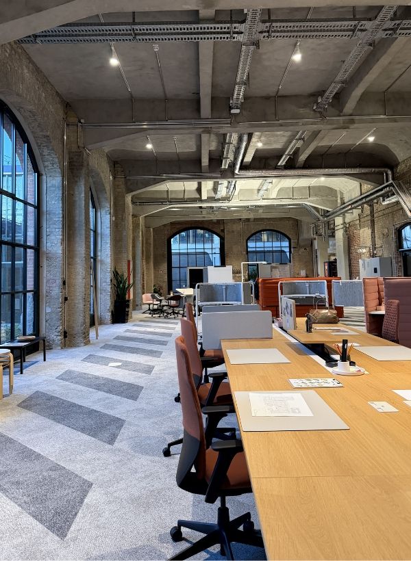 Offene Arbeitslandschaft im Vitra BETA Event Space mit gemeinsamen Arbeitsplätzen, akustisch abgeschirmten Bereichen und historischer Industriearchitektur.