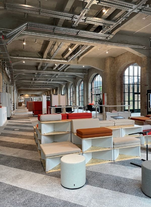 Modulare Sitzlandschaft mit integrierten Regalen, Loungebereichen und Arbeitszonen im Vitra BETA Event Space innerhalb einer historischen Industriehalle.