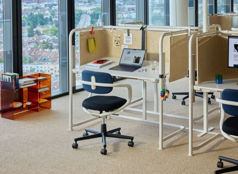 Agile Einzelarbeitsplätze mit halbhohen Trennwänden vor einer Fensterfront; Schreibtische, Bürostühle und Sichtschutz schaffen abgeschirmte Arbeitsbereiche in offener Umgebung.