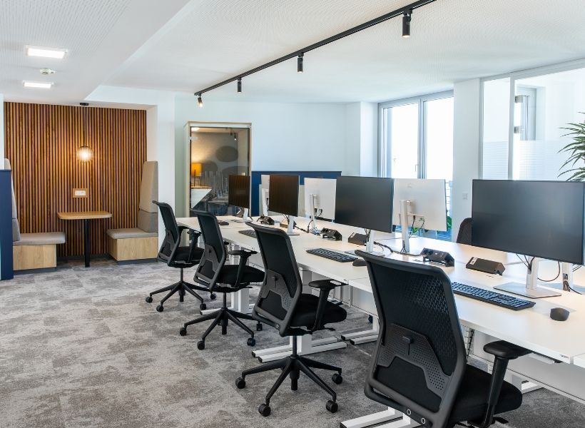 Offene Bürofläche mit ergonomischen Arbeitsplätzen, klarer Struktur und akustisch wirksamem Rückzugsbereich für konzentriertes Arbeiten.