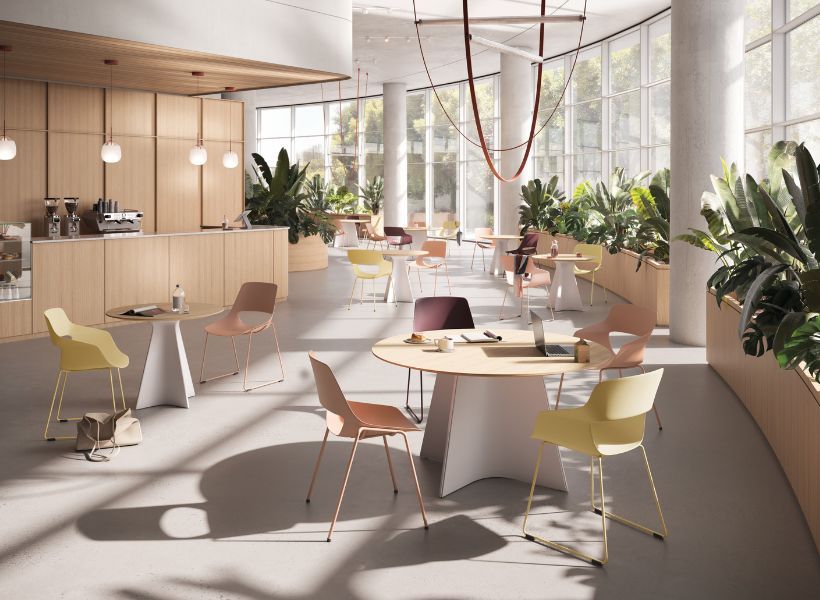 Großzügiges Workcafé mit Kaffeetheke, runden Besprechungstischen, Arbeitsplätzen und bepflanzten Sitzbereichen entlang großer Fensterfronten.