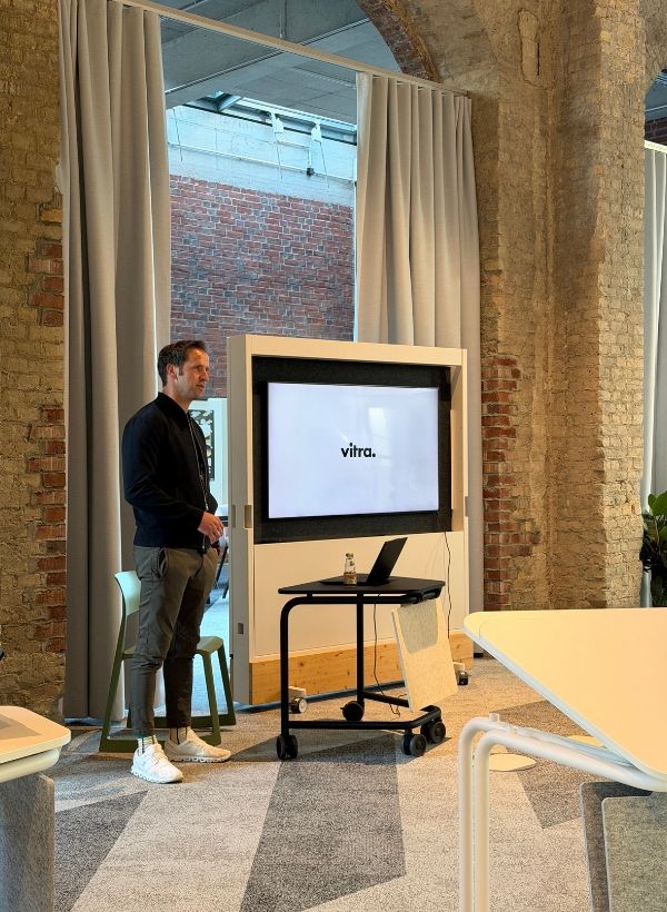 Präsentationssituation im Vitra BETA Event Space mit mobilem Bildschirm, Besprechungstisch und flexibler Fläche für Workshops und Veranstaltungen.