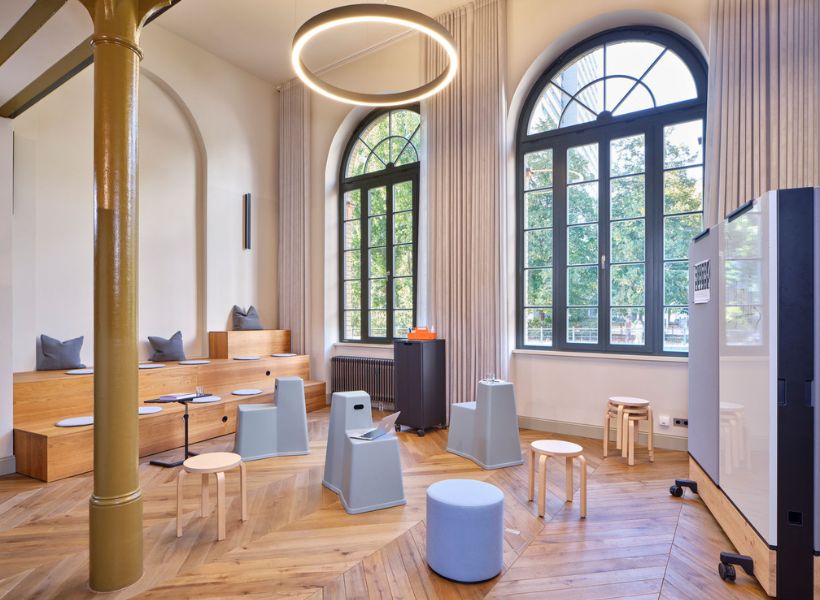 Workshop- und Besprechungsbereich mit großzügigem Tageslicht, ringförmiger Pendelleuchte und zonierter Beleuchtung für unterschiedliche Nutzungen.