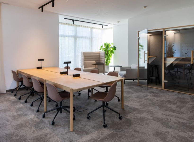 Besprechungsbereich mit großem Holztisch, gerichteter Arbeitsplatzbeleuchtung, ergänzendem Tageslicht und integrierten Rückzugszonen.