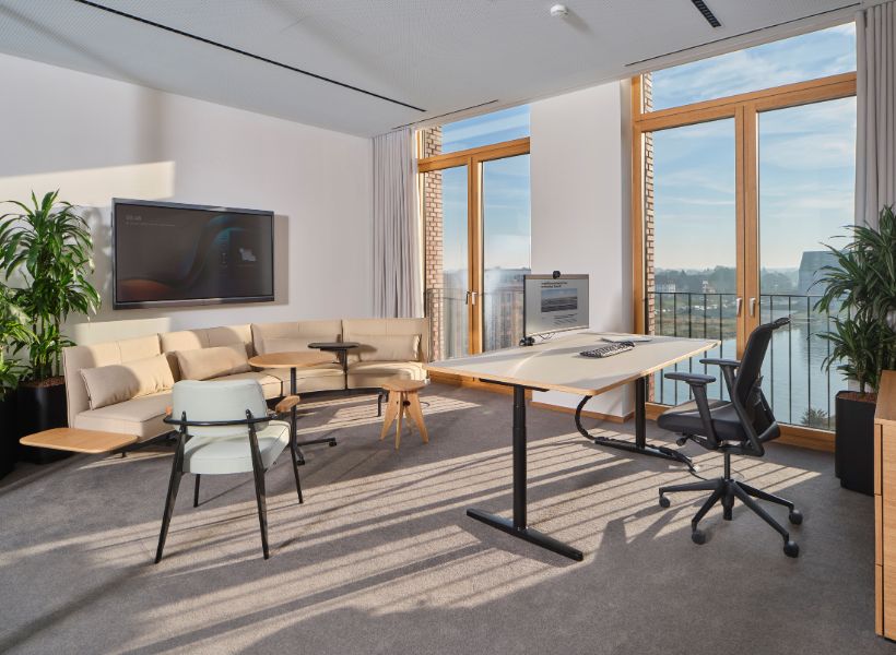 Open-Space-Büro mit großzügigem Tageslicht, höhenverstellbaren Arbeitsplätzen und zonierter Struktur für konzentriertes Arbeiten und Austausch.